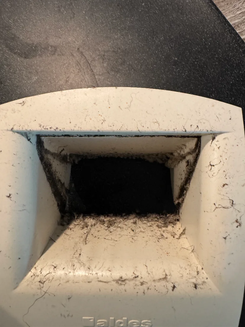 Bouche de VMC déposée, poussières et fibres accumulées autour du passage d’air